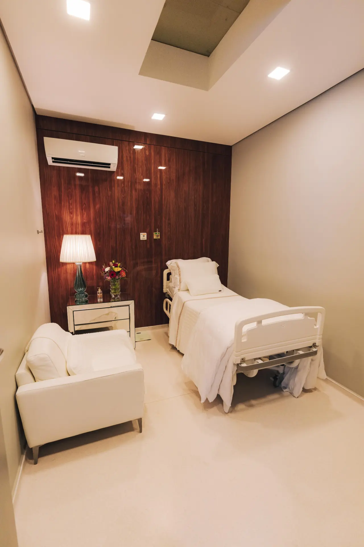 Quarto de internação com leito hospitalar, poltrona e painel em madeira nobre